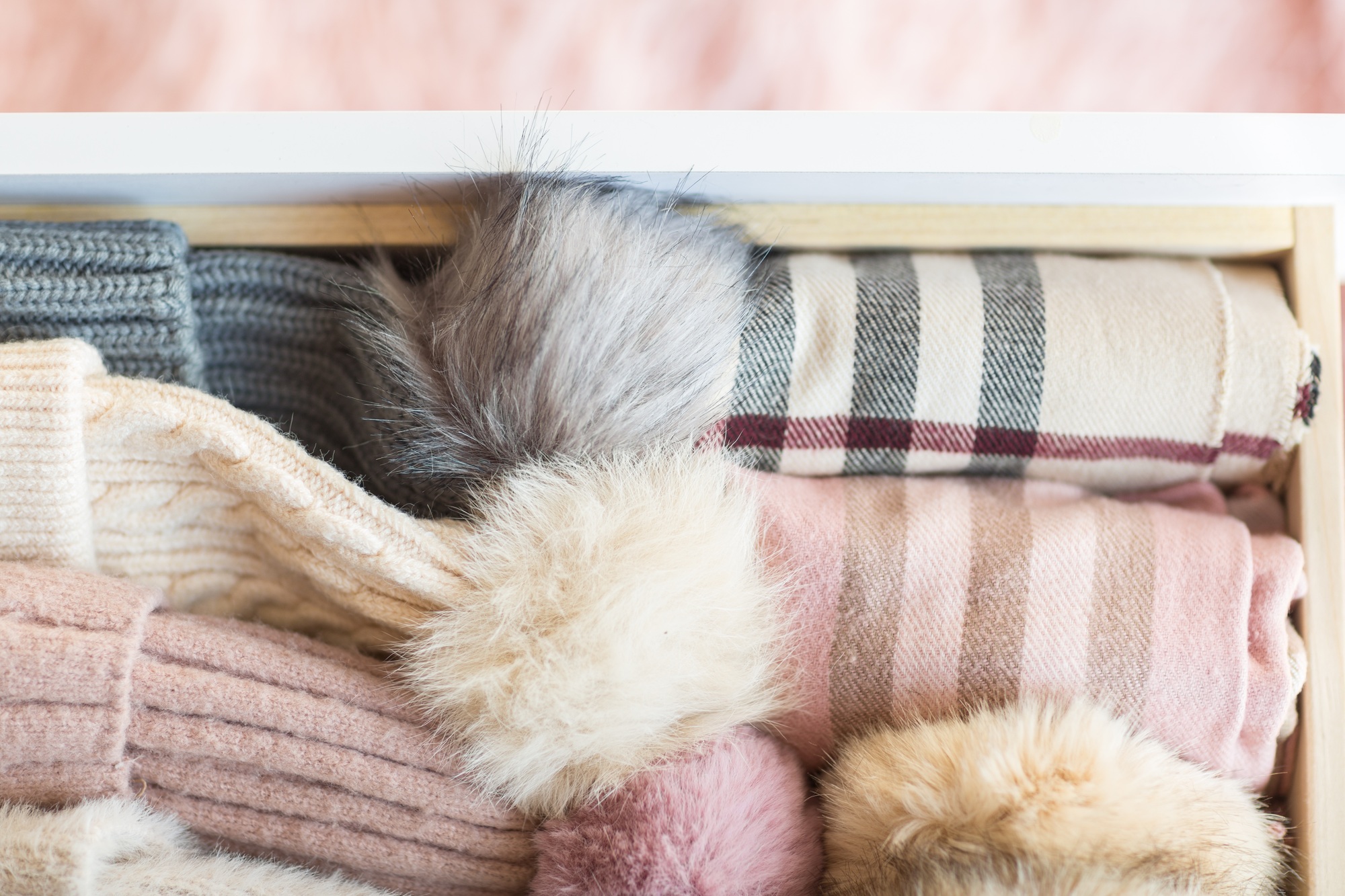 Cozy knitted woolen hats with pompons and scarves in wardrobe. Neutral pastel colors, winter season