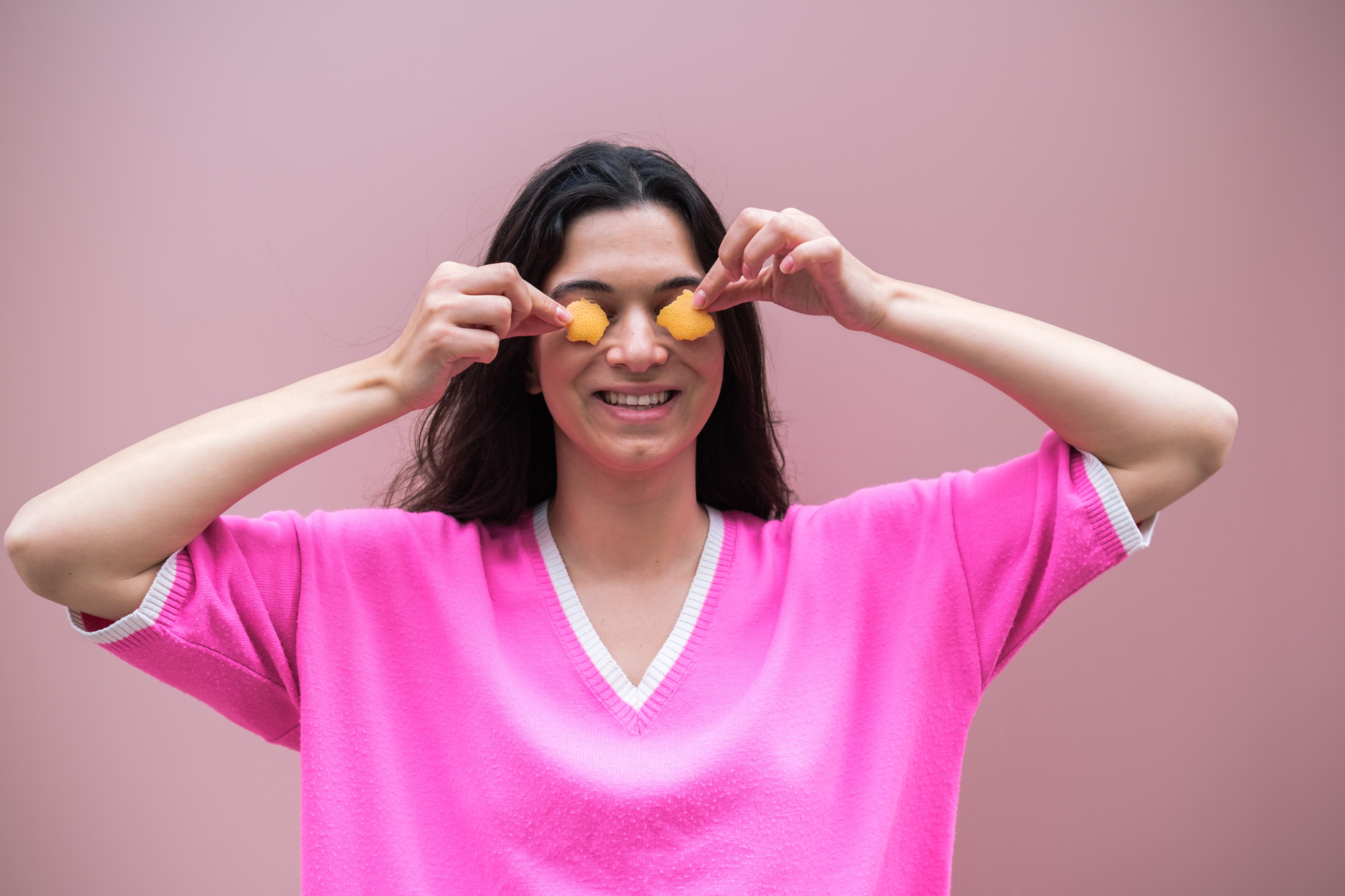 Smiling woman holding orange slices on eyes for beauty treatment